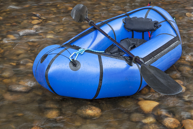 a blue packraft (one-person light raft used for expedition or adventure racing) with a kayak paddle against a shallow river