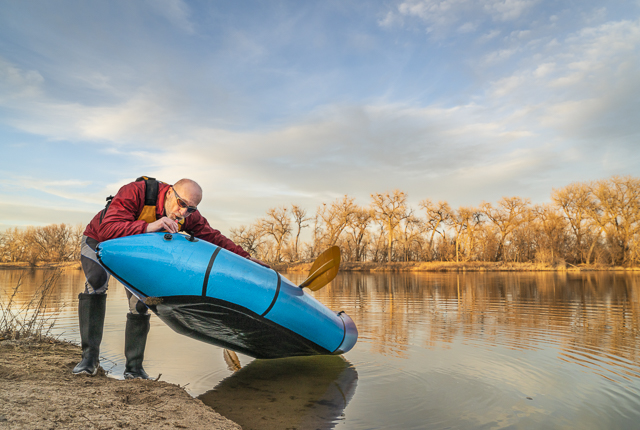 senior male paddler is adding air to an inflatable packraft