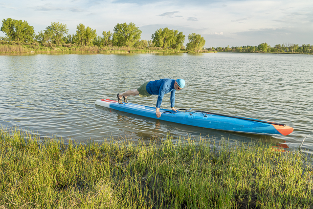 senior paddler is warming up by doing pushups before workout on a stand up paddleboard