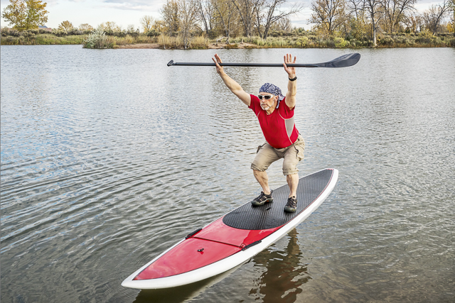 senior male paddler stretching and warming up on a paddleboard before paddling workout on a lake in Colorado