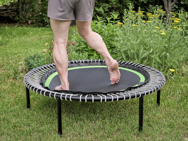 rebounding concept - feet and legs of a muscular man jumping on a mini trampoline in a backyard