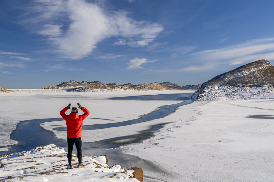 male hiker in down jacket on a rocky shore of frozen Horsetooth Reservoir in northern Colorado
