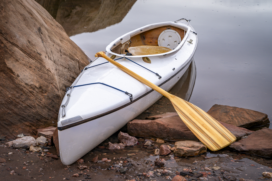 decked expedition canoe with a wooden paddle on a rocky shore of Horsetooth Reservoir near Fort Collins, Colorado, low water level fall or winter scenery