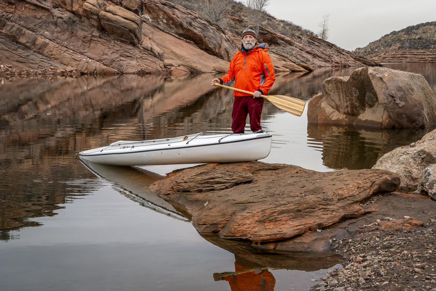 senior male paddler with a decked expedition canoe with a wooden paddle on a rocky shore of Horsetooth Reservoir near Fort Collins, Colorado, low water level fall or winter scenery