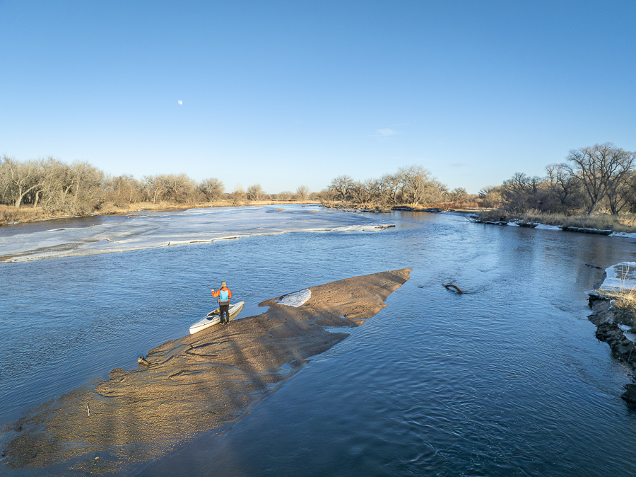 male paddler with a decked expedition canoe on a sandbar with ice floe - South Platte River in eastern Colorado