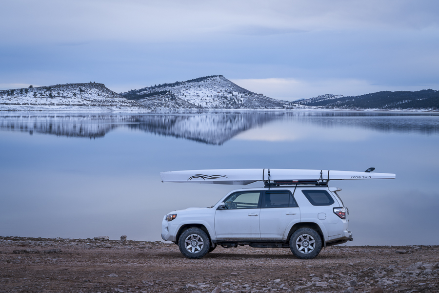 Loveland, CO, USA - February 6, 2024: Toyota 4Runner SUV with Liteboat rowing shell on roof racks on a shore of Carter Lake in northern Colorado at winter dusk.