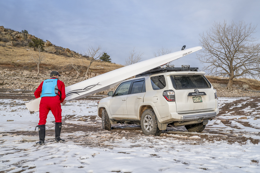 Loveland, CO, USA - February 6, 2024: Senior rower is loading Liteboat rowing shell on roof racks of Toyota 4Runner SUV on a shore of Carter Lake in northern Colorado in winter scenery.